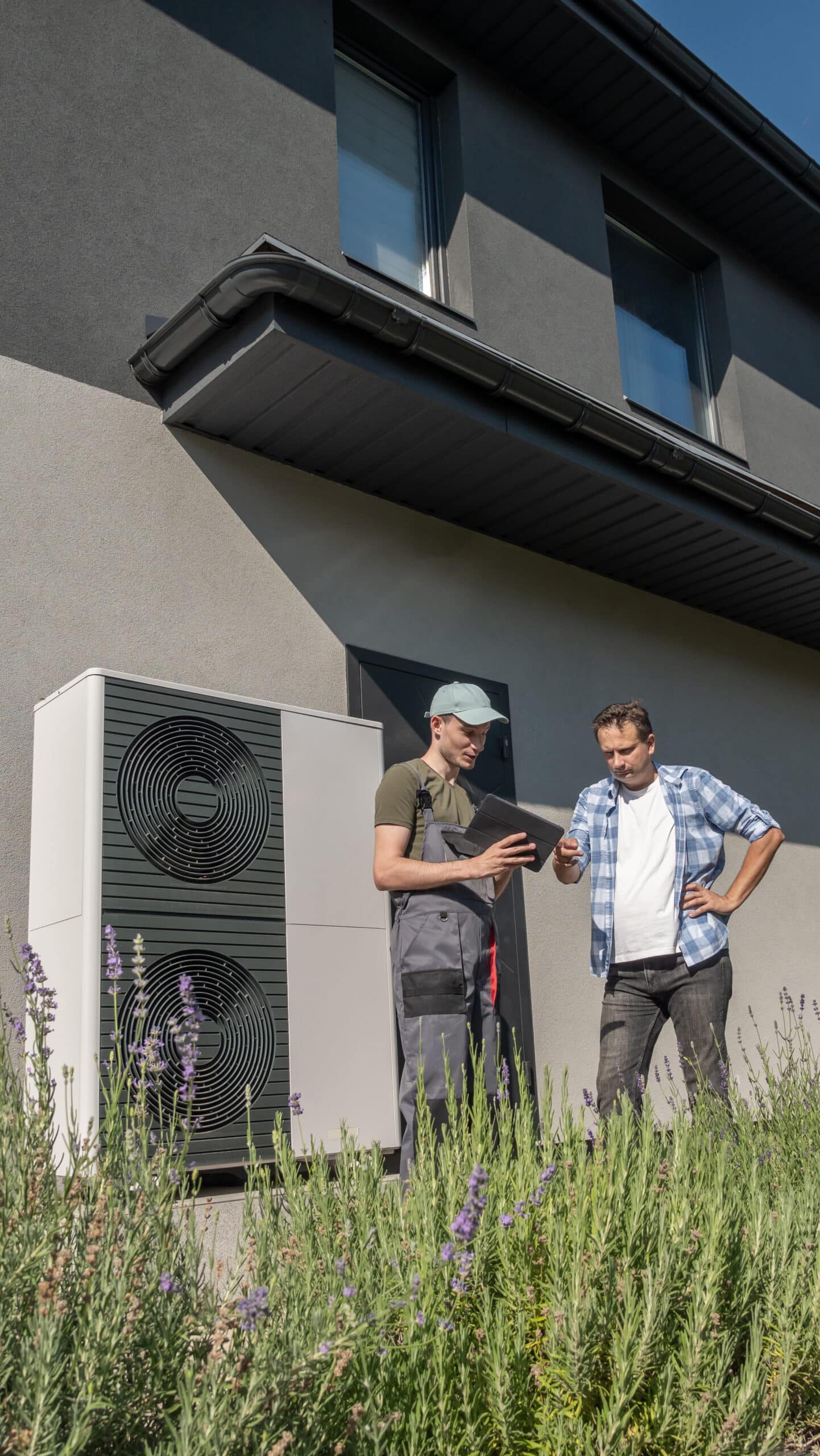 technician homeowner discussing heat pump maintenance outside house with heat pump unit scaled